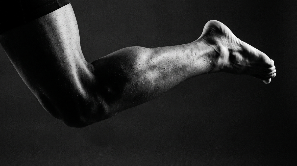 Dark cinematic black-and-white close-up photograph of calf muscles mid-jump