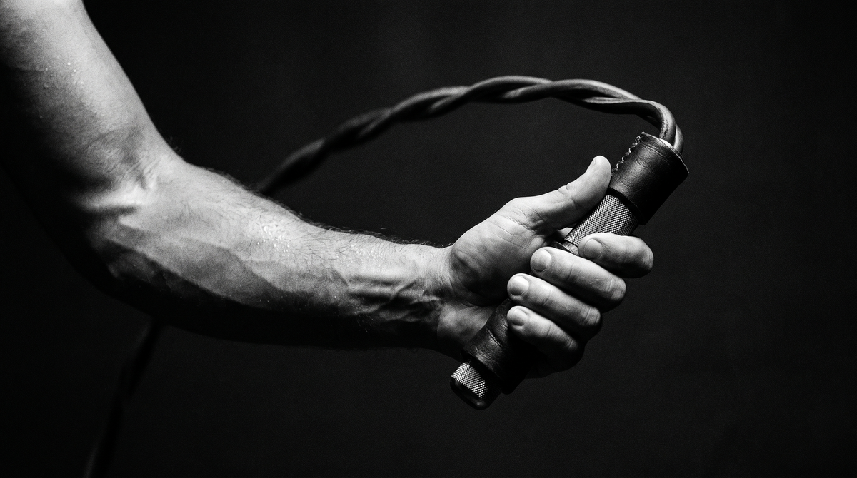 Dark cinematic black-and-white close-up photograph of a hand gripping a weighted jump rope handle