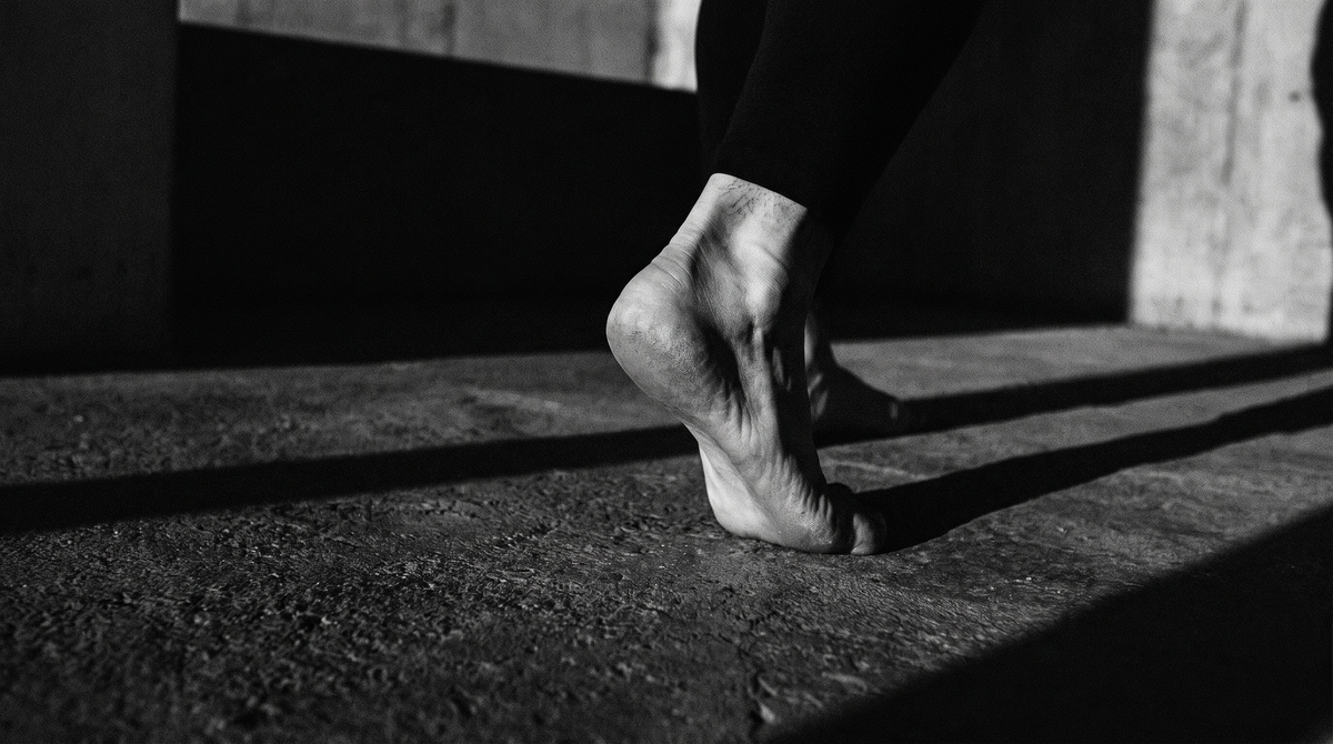 Black and white cinematic photo of a bare heel striking dark concrete mid-jump, motion blur, dramatic shadow