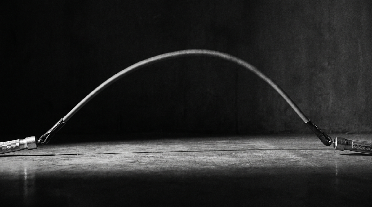Black and white editorial photograph of a weighted jump rope frozen mid-swing in a dark minimal studio