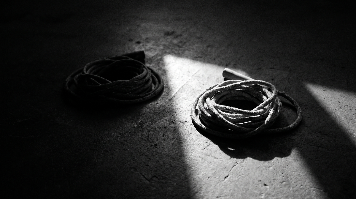 Black and white editorial photograph of two jump ropes coiled on a dark concrete studio floor, one lit and one in shadow